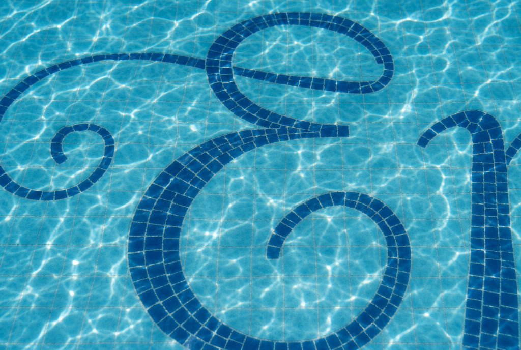 Macro study — the pool's mosaic letterform under rippling water