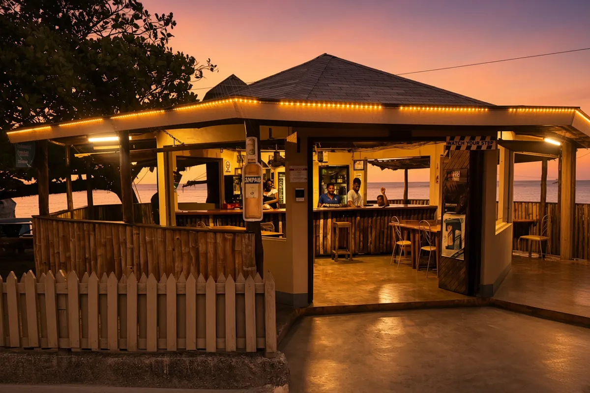 An open-sided bar lit warm against an orange sunset, thatched roof and picket fence facing the water