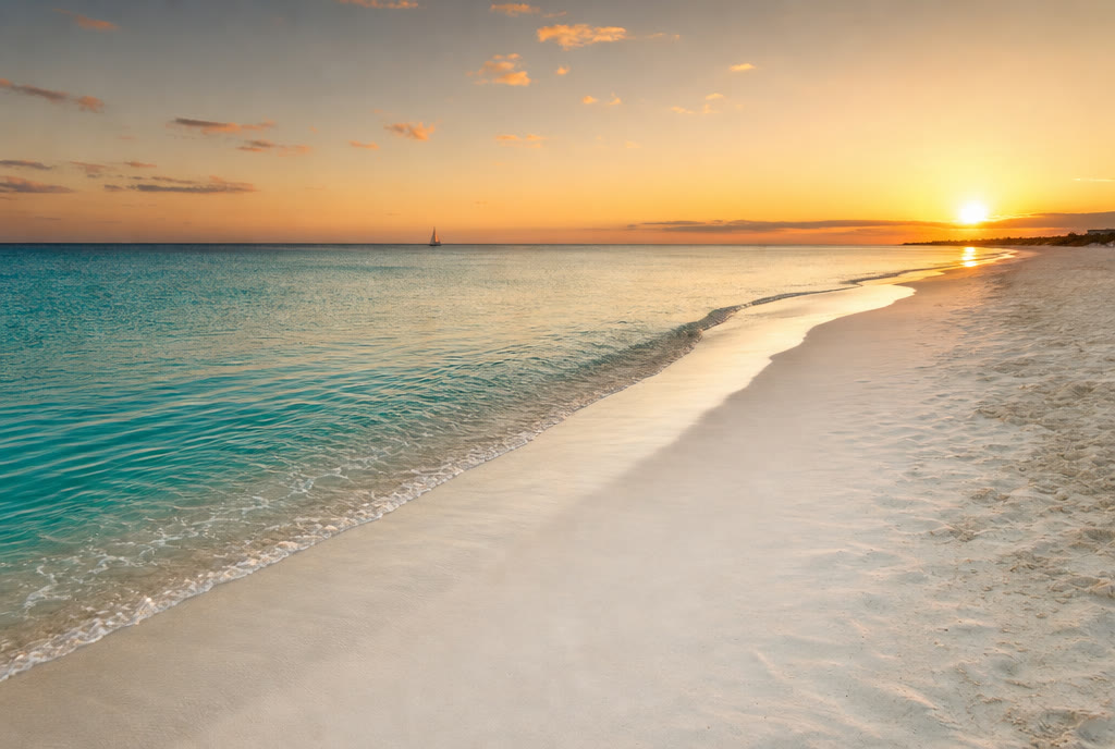 A long empty Caribbean beach at sunset, calm turquoise water and amber sky